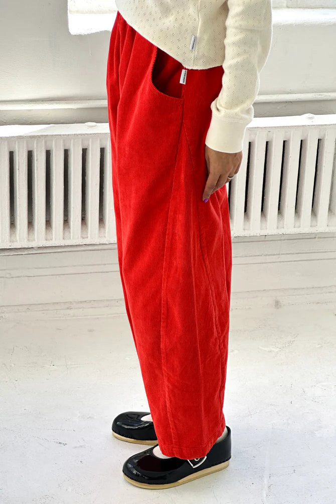 Woman wearing bright red Arc pants from Le Bon Shoppe and a white top in a minimalistic setting.
