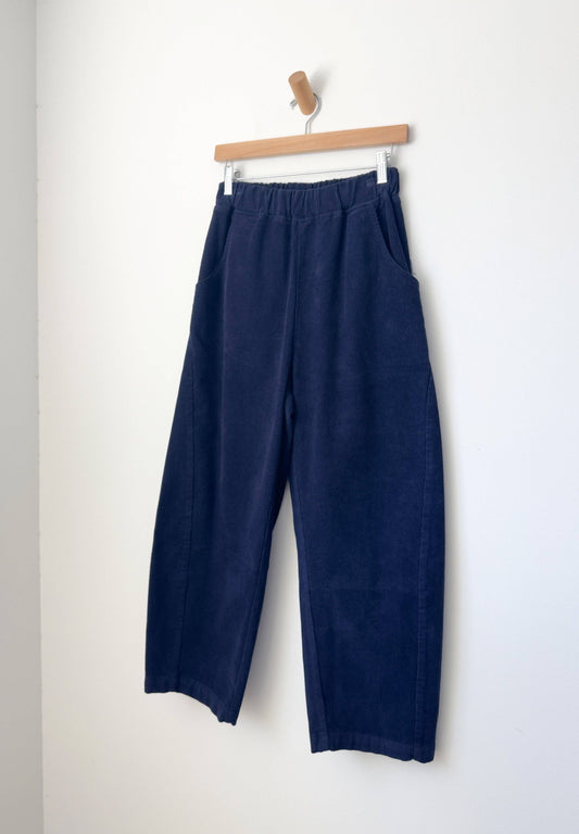 Navy blue corduroy Le Bon Shoppe Arc pants hanging on a wooden hanger against a white background