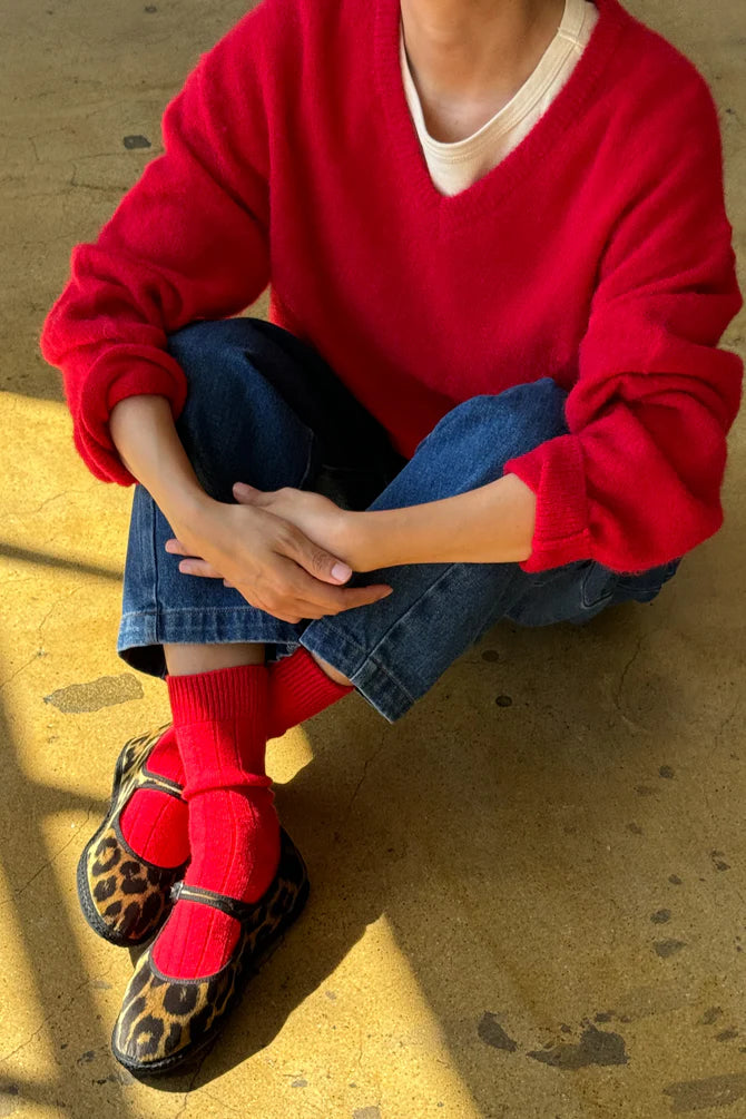 Person wearing the red James mohair blend jumper from Le Bon Shoppe, blue jeans, red socks, and leopard print shoes on a textured surface.