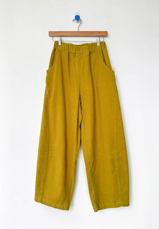Mustard yellow barrel leg corduroy Arc pants from Le Bon Shoppe hanging on a wooden hanger against a white background