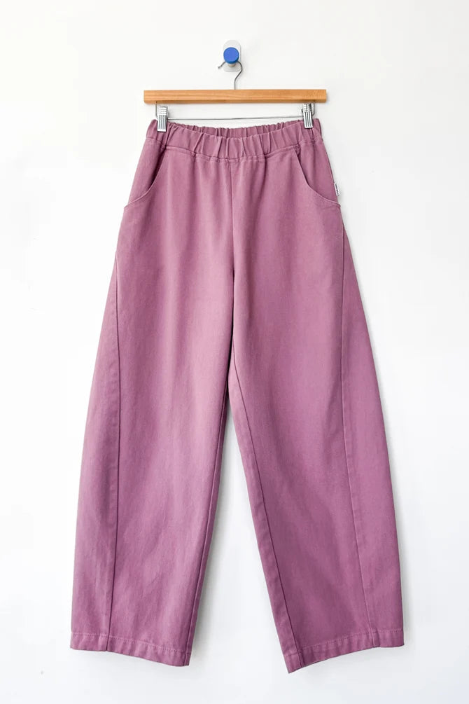A pair of wide-leg cropped Arc pants by Le Bon Shoppe in a dusty mauve or muted purple color, hanging from a wooden hanger against a plain white wall.