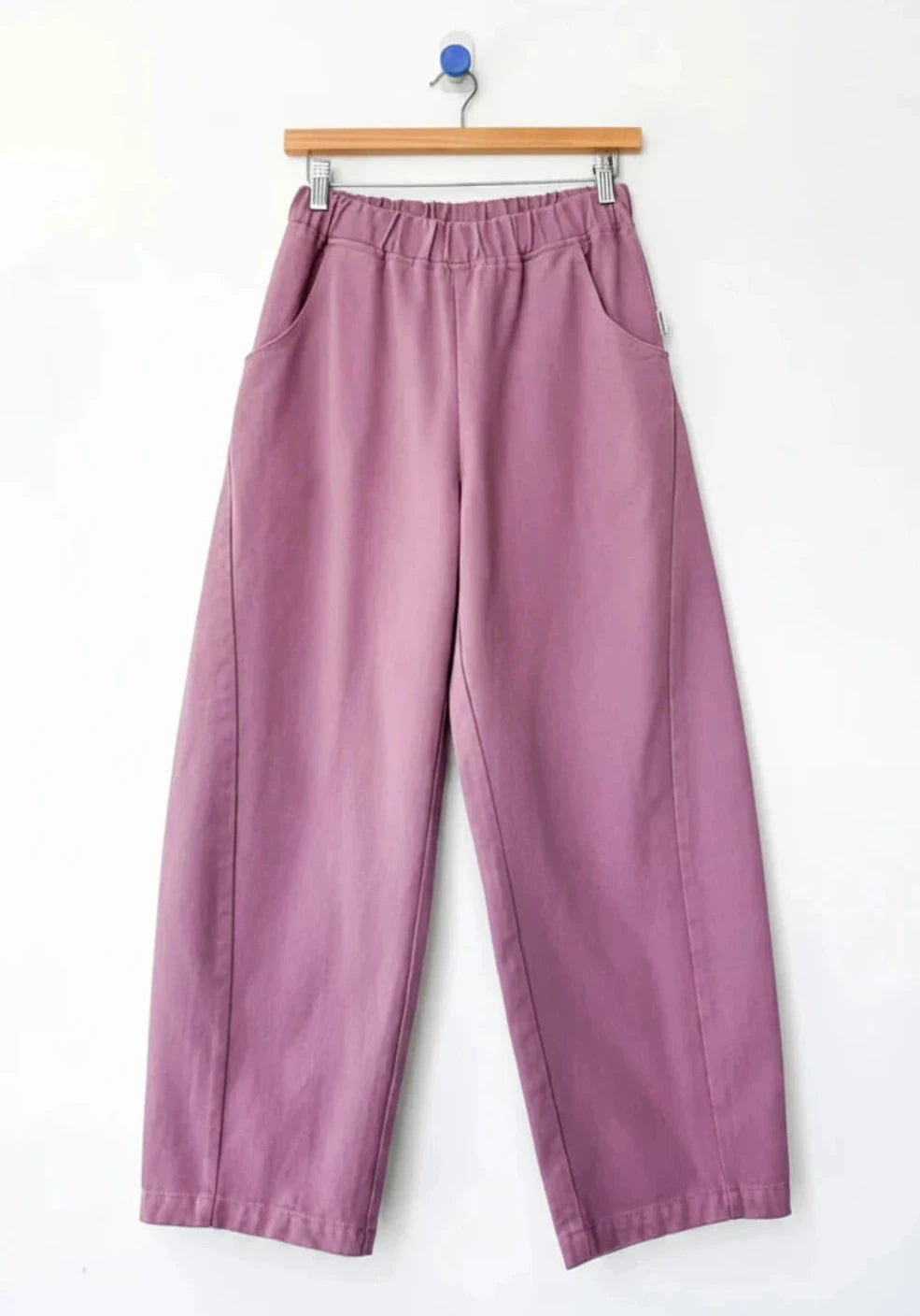 A pair of wide-leg cropped Arc pants by Le Bon Shoppe in a dusty mauve or muted purple color, hanging from a wooden hanger against a plain white wall.