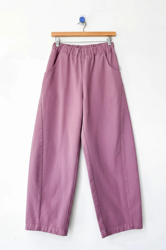 A pair of wide-leg cropped Arc pants by Le Bon Shoppe in a dusty mauve or muted purple color, hanging from a wooden hanger against a plain white wall.