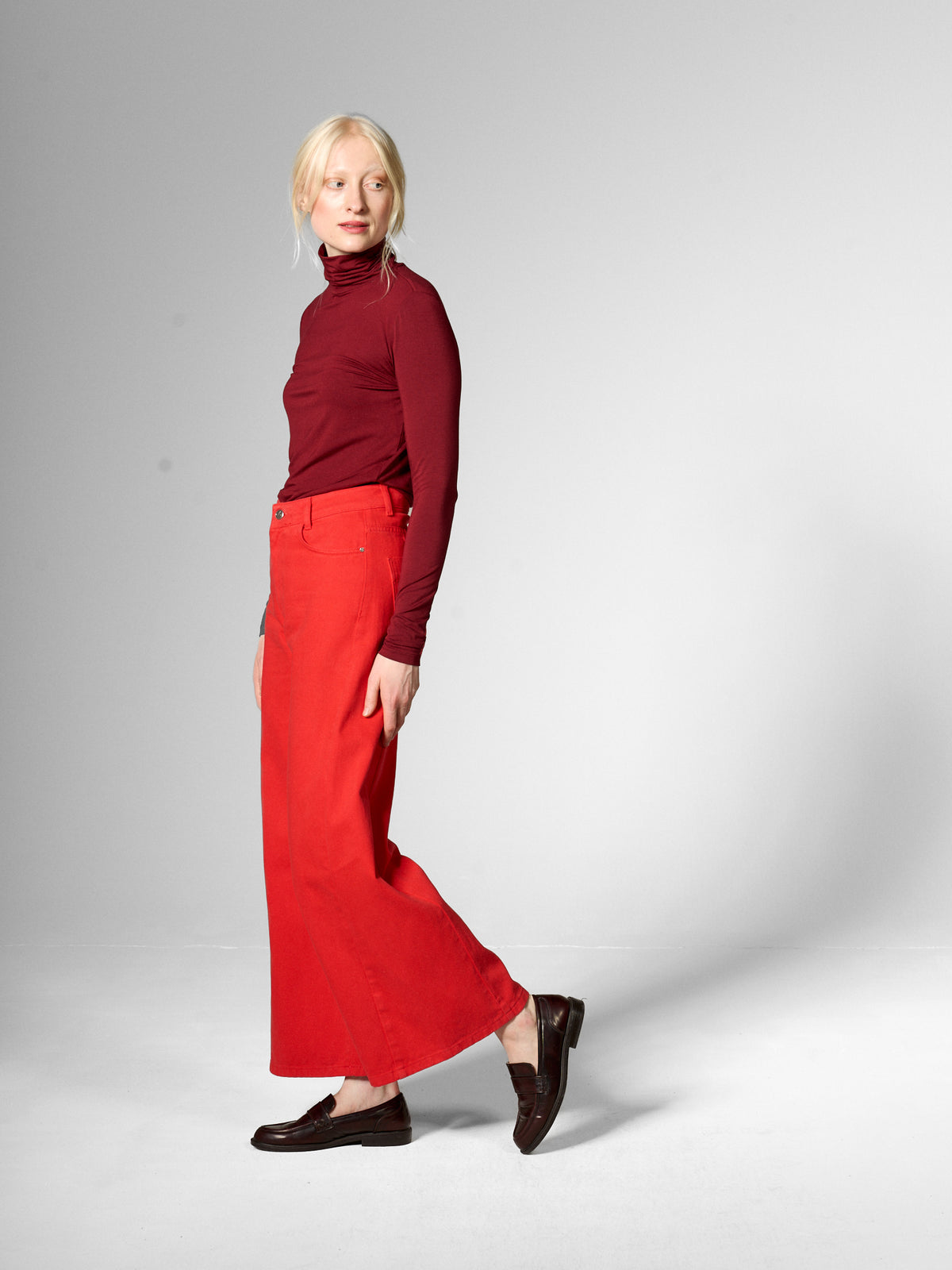 A woman wearing a wine red turtle neck top and bright red wide leg trousers from Mademoiselle Yeye.
