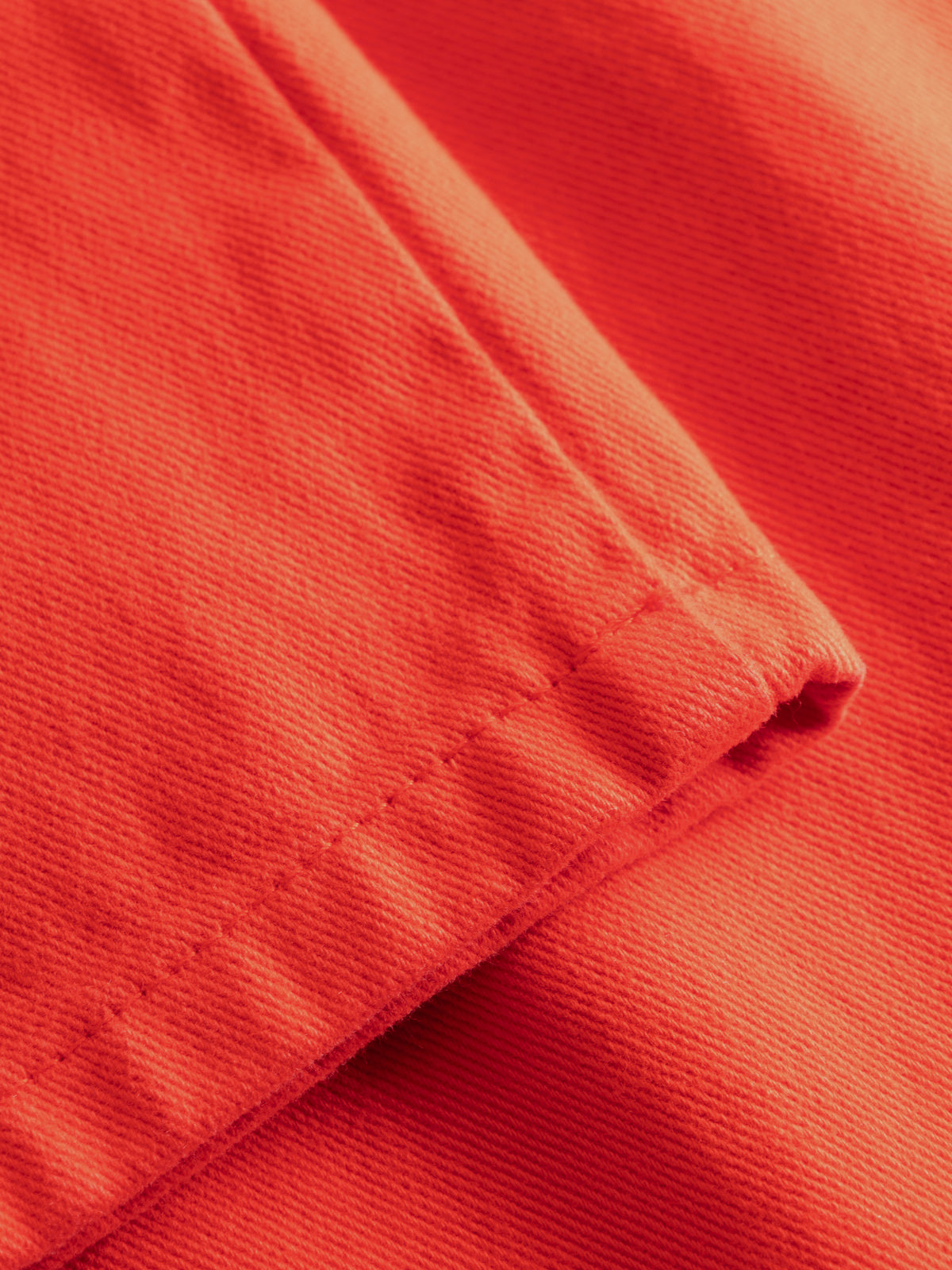 A close-up of bright orange-red woven fabric with visible texture and a folded seam.