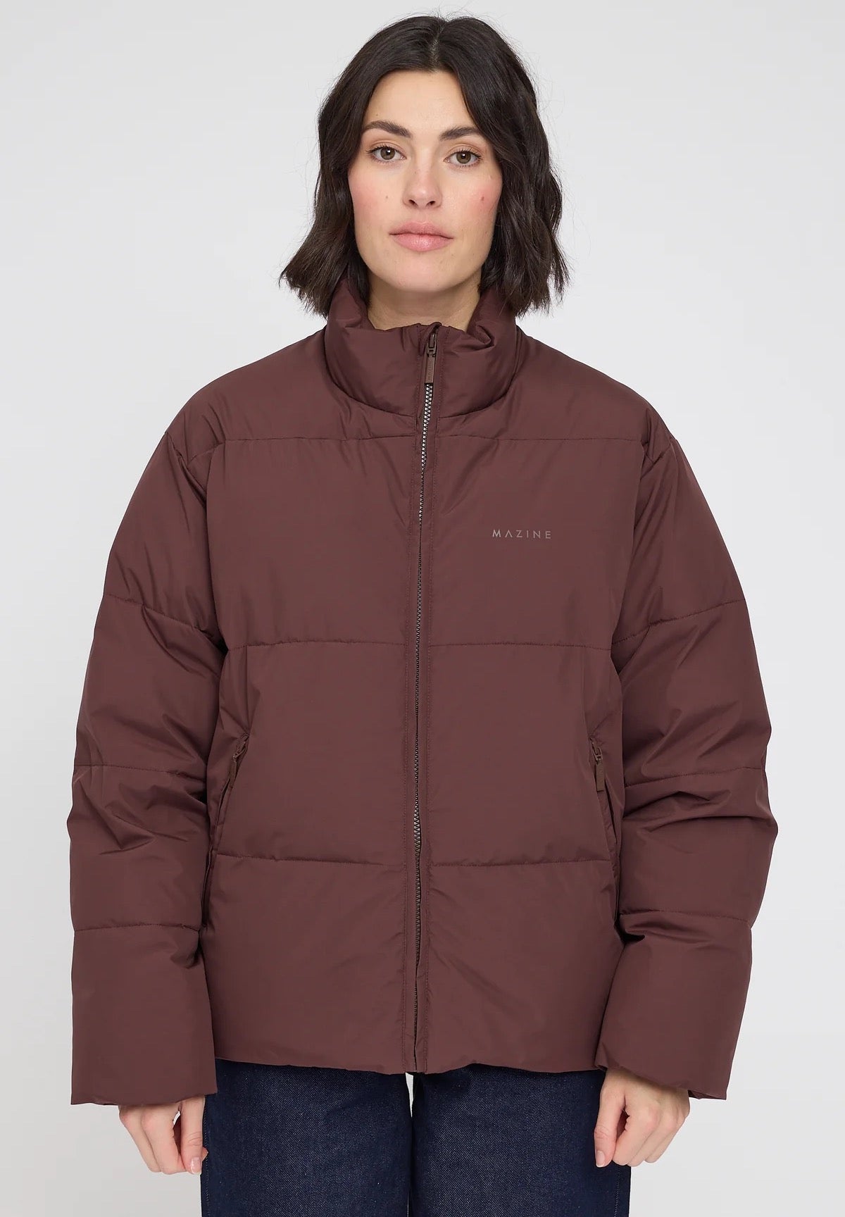 Woman wearing a chocolate brown puffer jacket with a visible brand logo on a white background