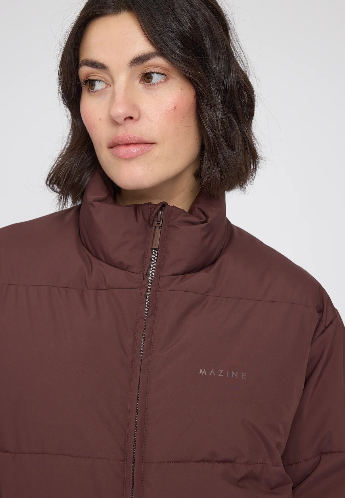 Woman wearing a chocolate brown loose fit puffer jacket with 'Mazine' branding on a white background