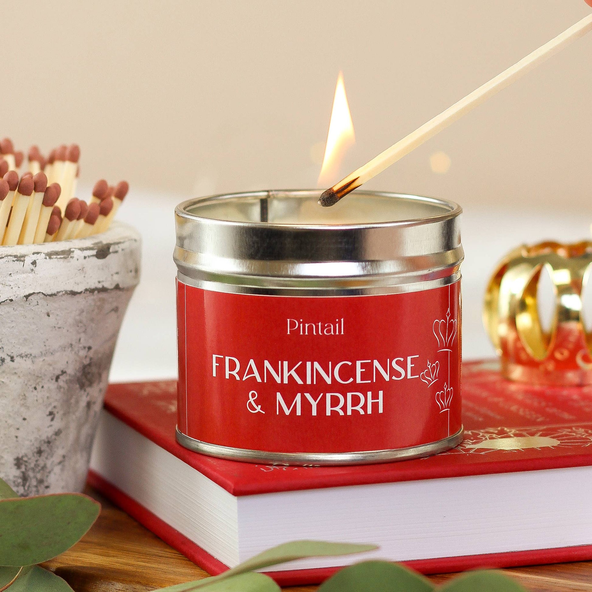 Candle labeled 'Frankincense & Myrrh' being lit with matches on a red book