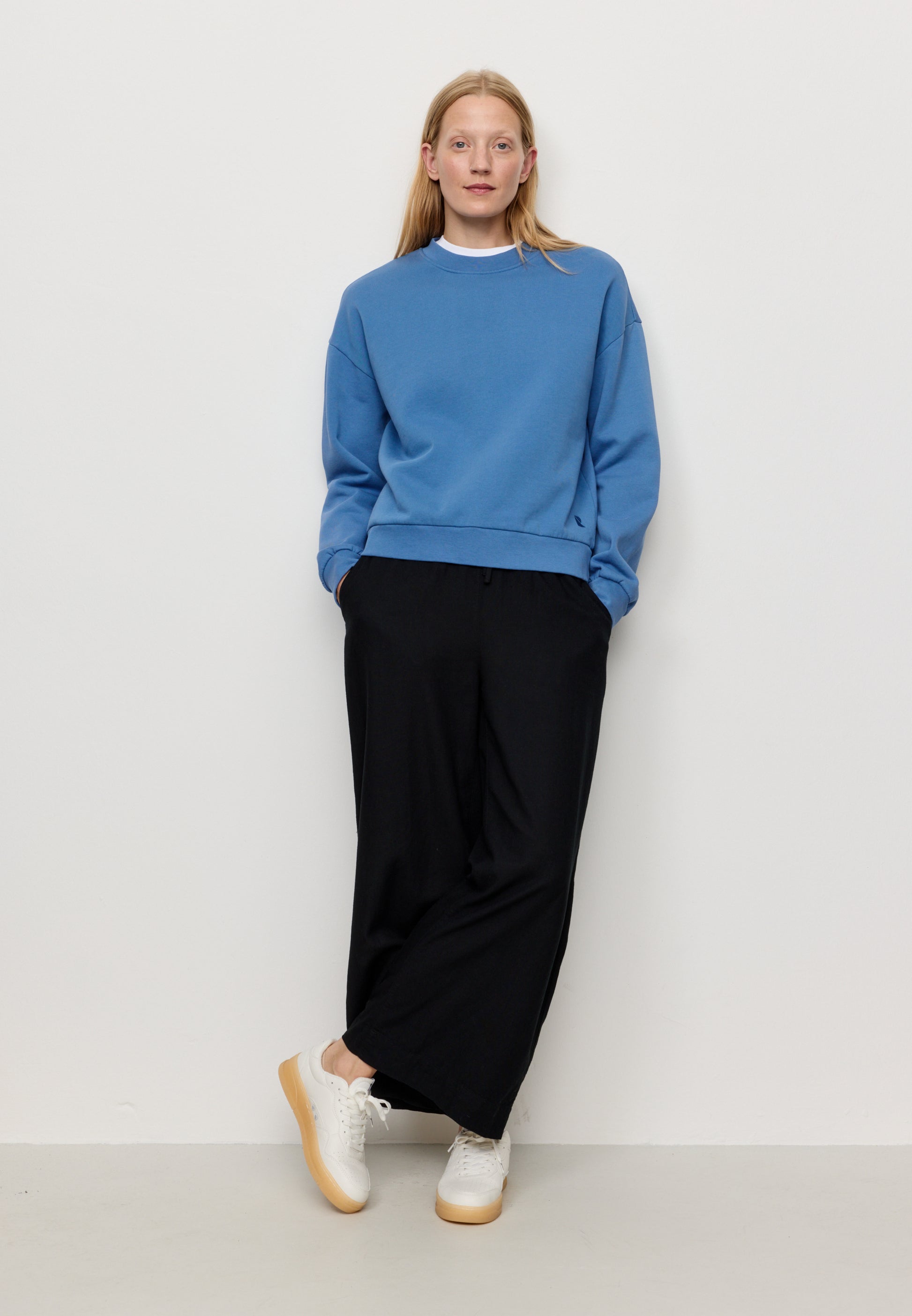 Woman wearing a blue sweatshirt and black pants against a white background