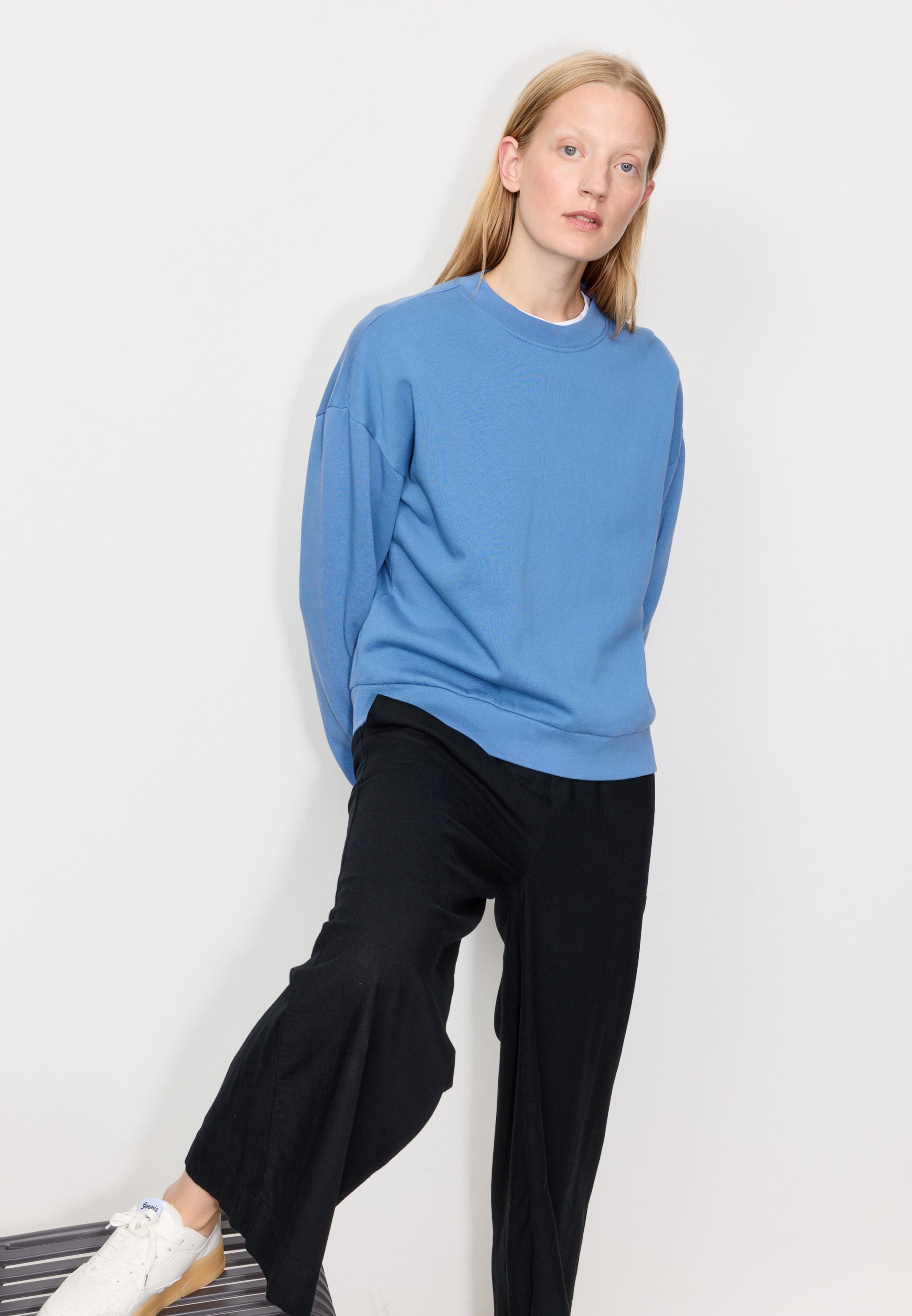 Woman wearing a blue sweater and black pants against a white background