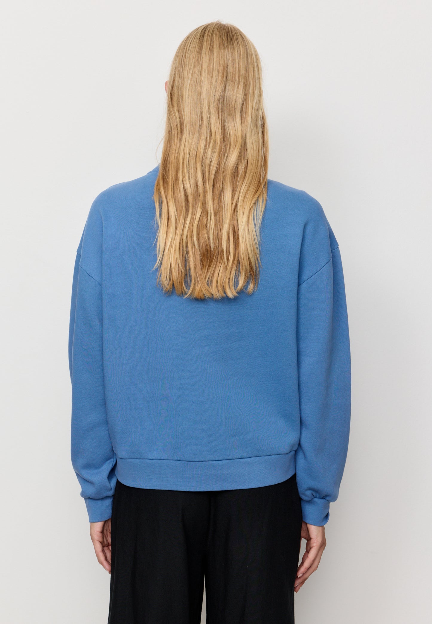 Woman wearing a blue sweatshirt from behind on a plain background