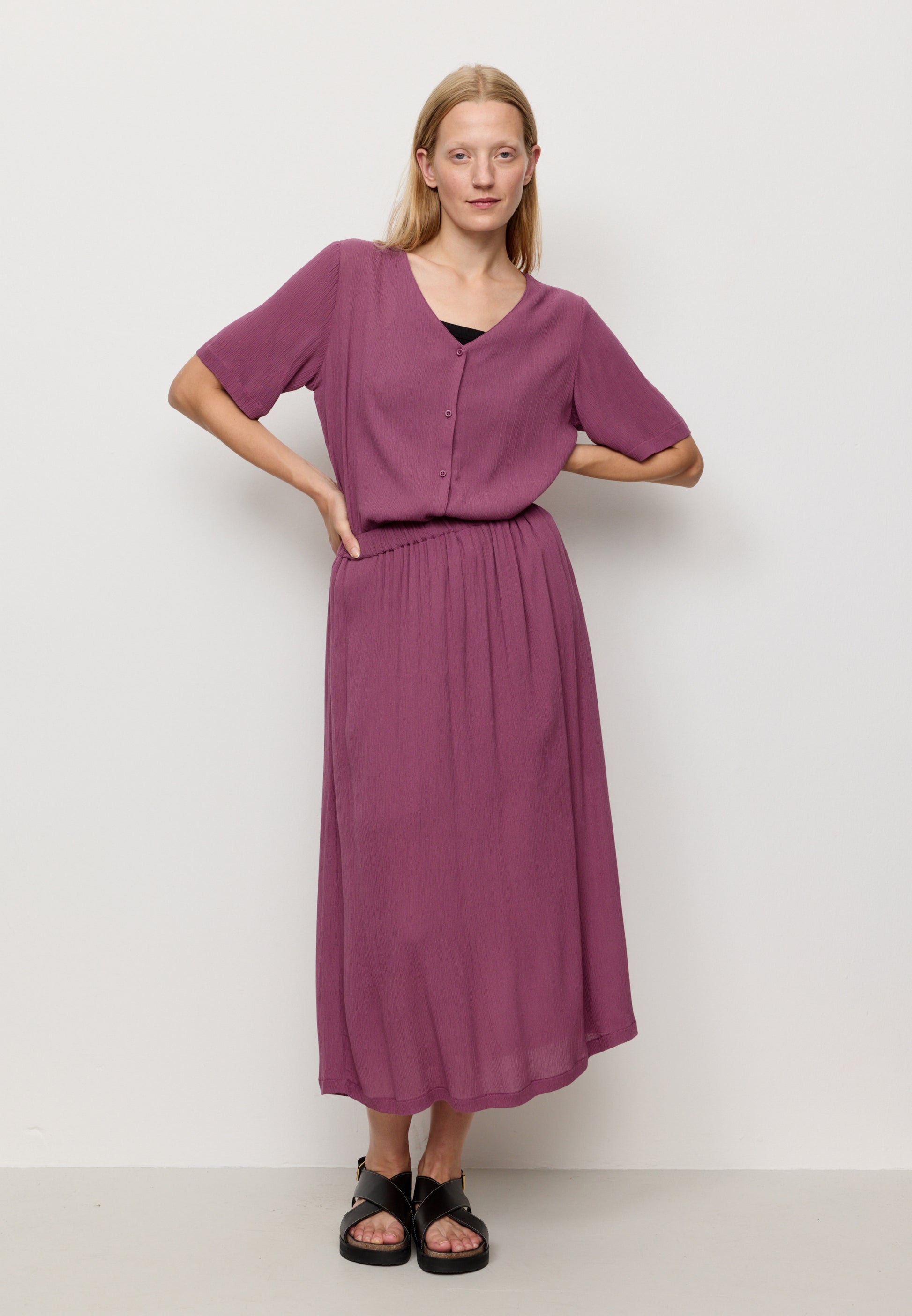 Woman wearing a purple skirt with a matching top with a plain background