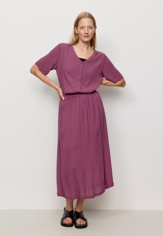 Woman wearing a purple skirt with a matching top with a plain background