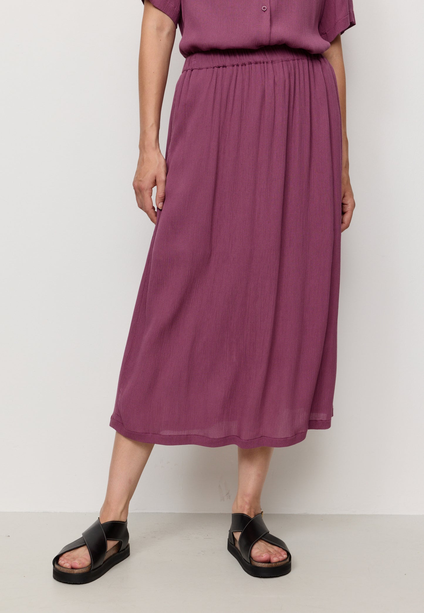 Person wearing a purple outfit with a skirt and top against a white background