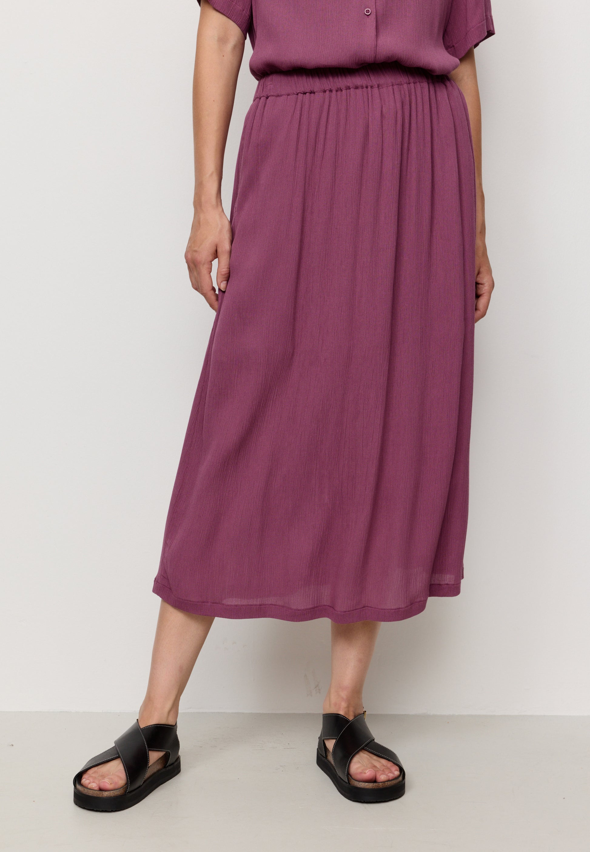 Person wearing a purple outfit with a skirt and top against a white background