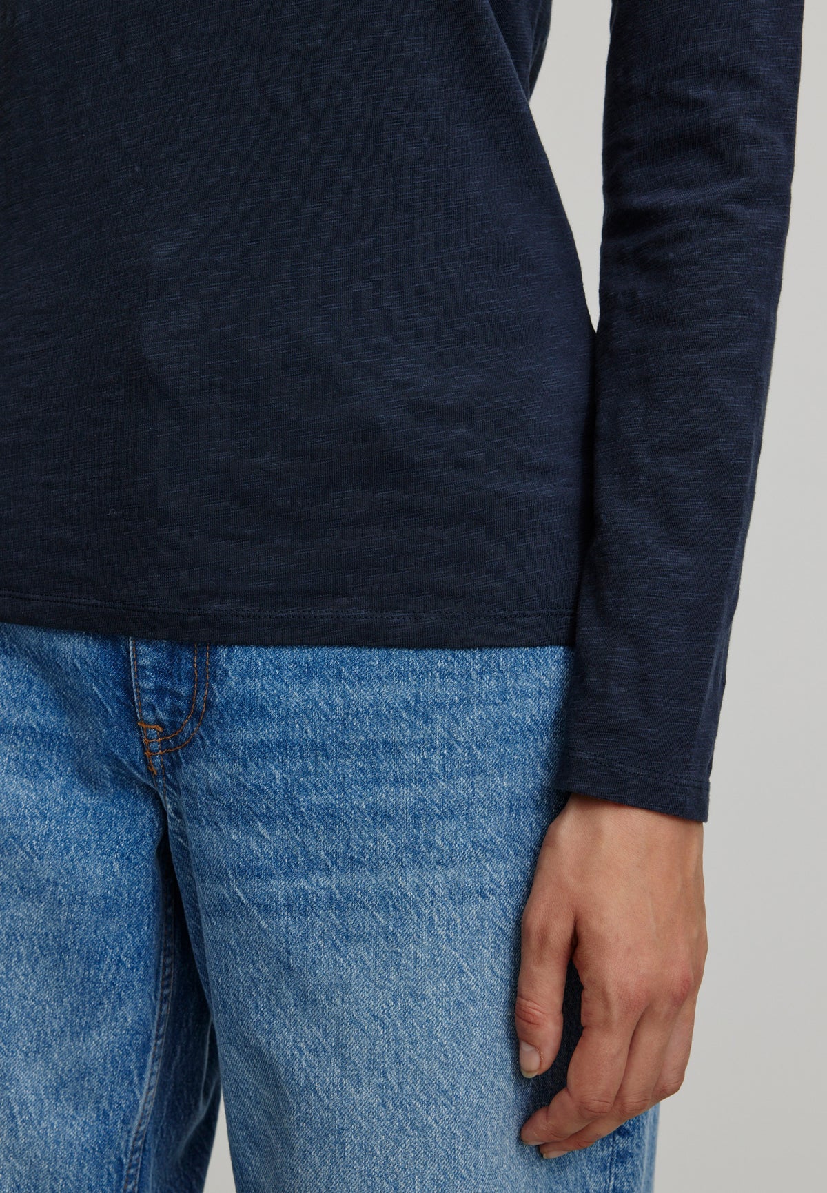 Woman wearing a navy long-sleeve shirt by Recolution and blue jeans on a light grey background