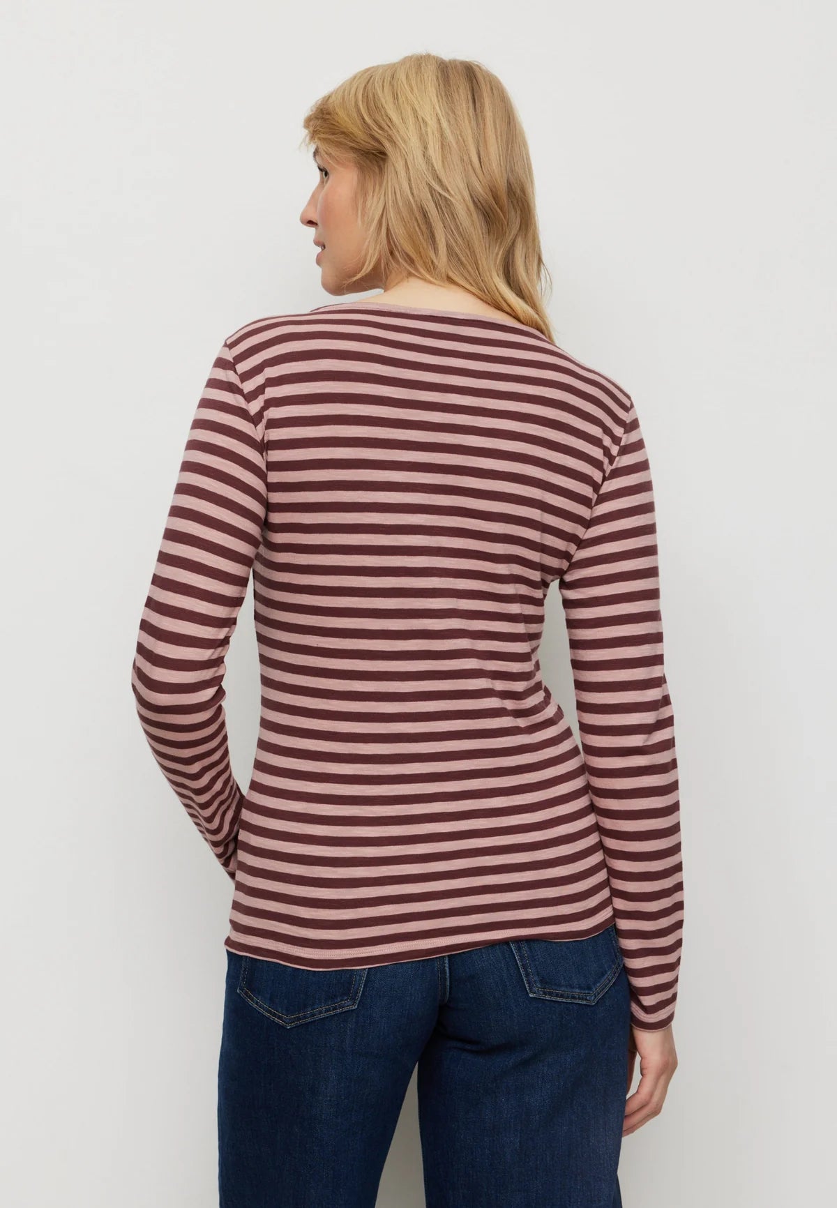 Woman wearing a striped long-sleeve shirt and jeans on a plain background