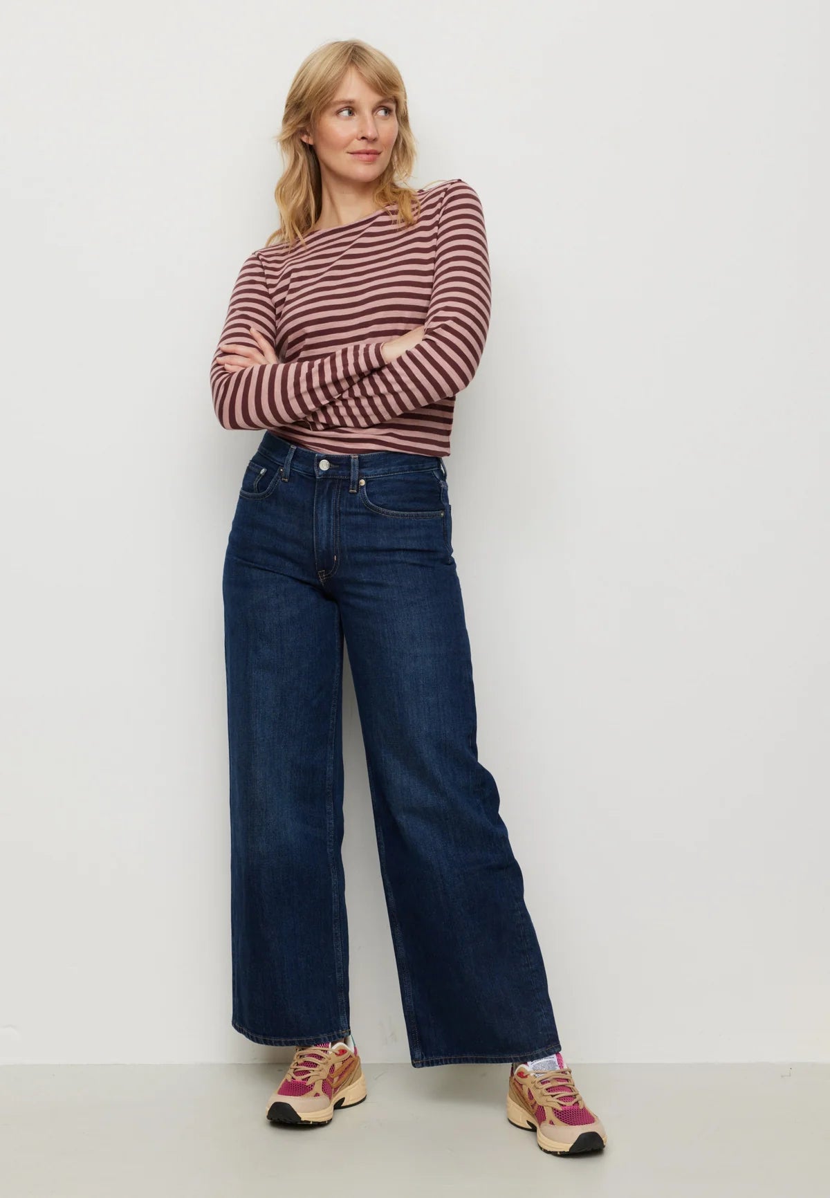 Woman wearing a striped sweater and blue jeans against a plain background