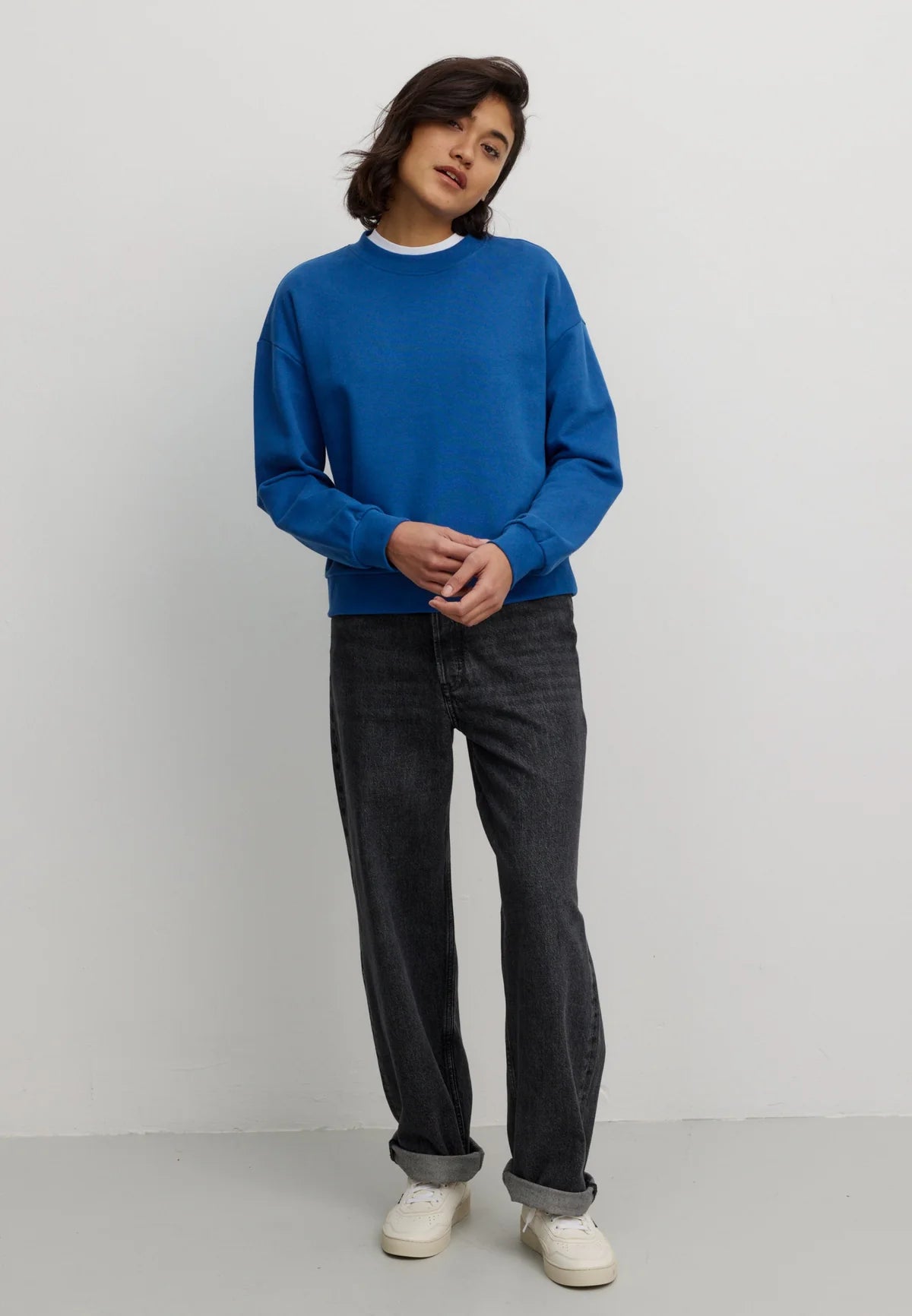 Woman wearing a blue organic cotton sweatshirt by Recolution and black pants against a white background