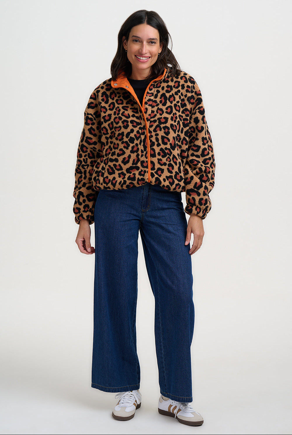 Woman wearing the Remi leopard print fleece jacket by Sugarhill Brighton with orange zipper and blue jeans on a white background