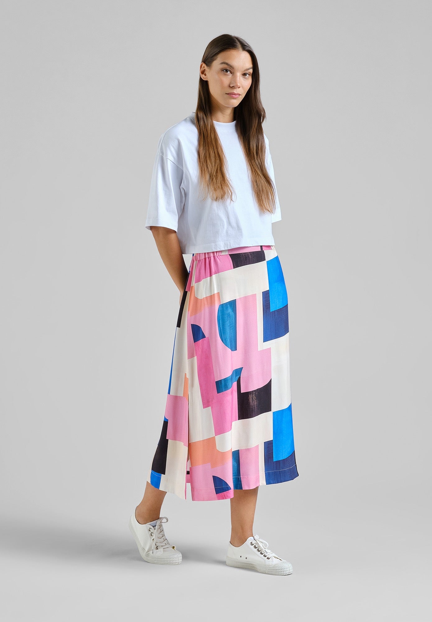 Woman wearing a white top and colorful geometric skirt on a gray background