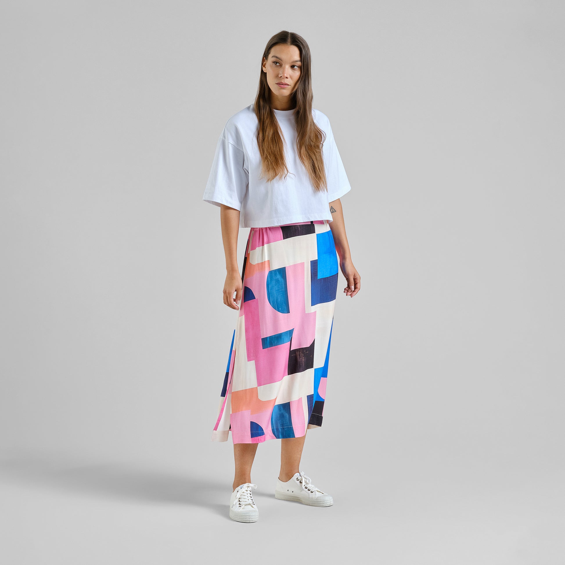 Woman wearing a colorful geometric skirt and white top on a gray background