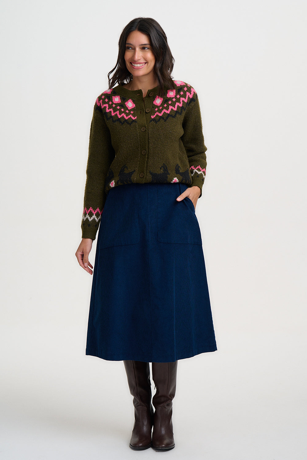 Woman wearing an olive green fair isle cardigan from Sugarhill Brighton with pink floral patterns and a blue skirt on a white background