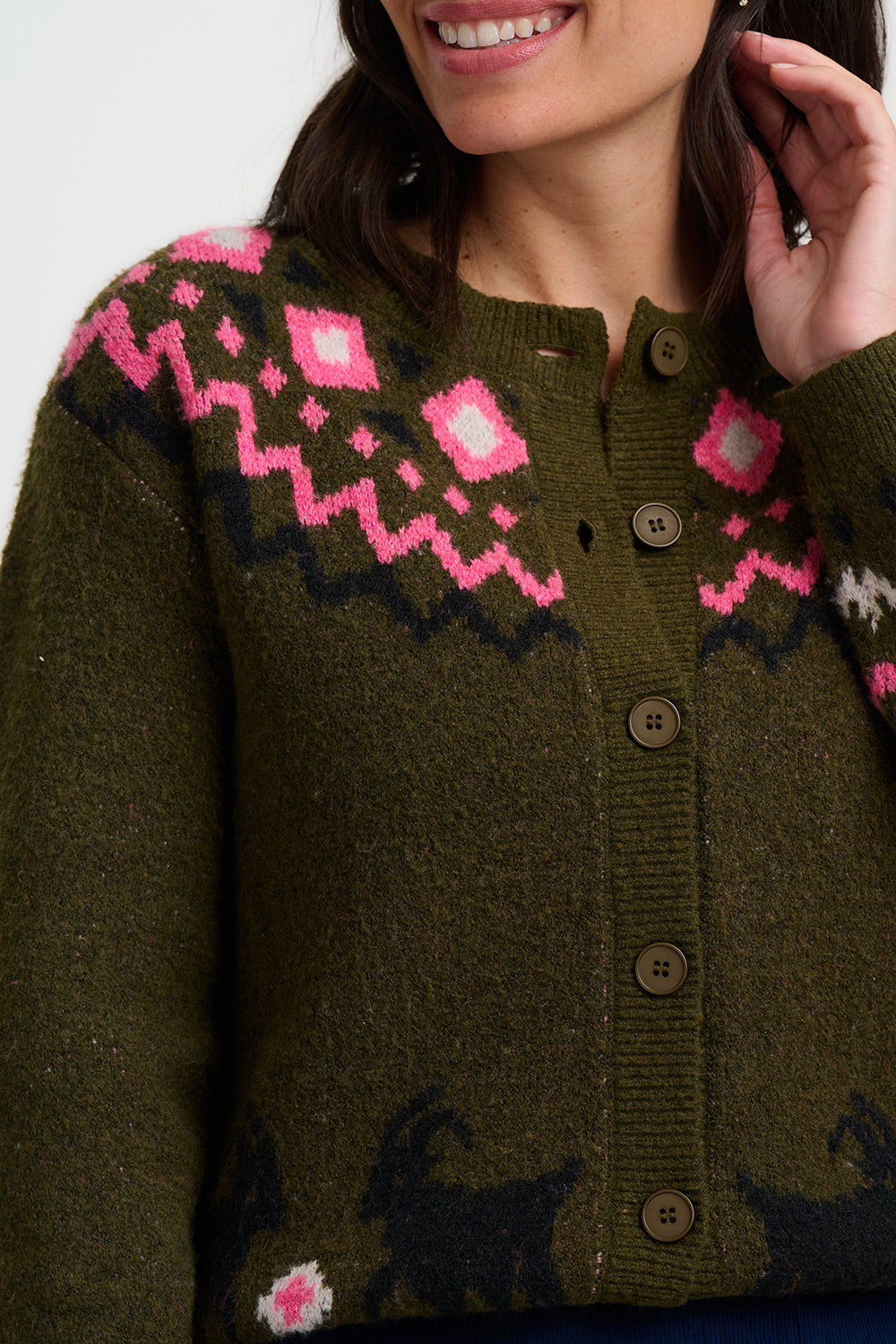 Person wearing an olive green cardigan from Sugarhill Brighton with a bright pink and black fair isle pattern