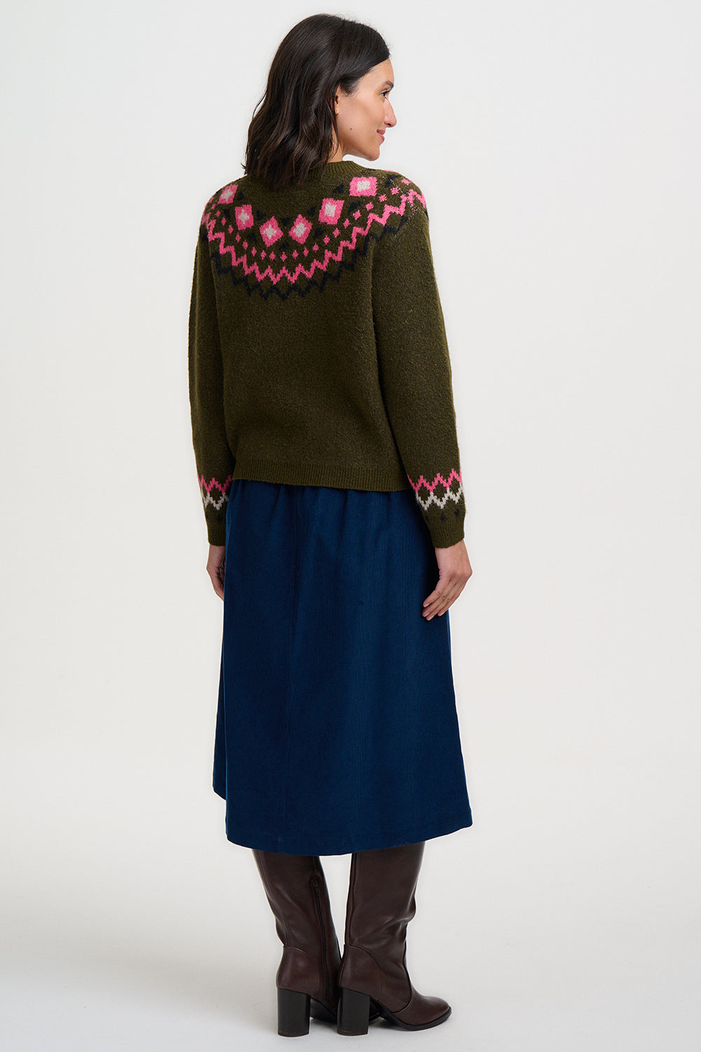 Woman wearing an olive green cardigan with a pink fair isle pattern and a blue skirt on a white background