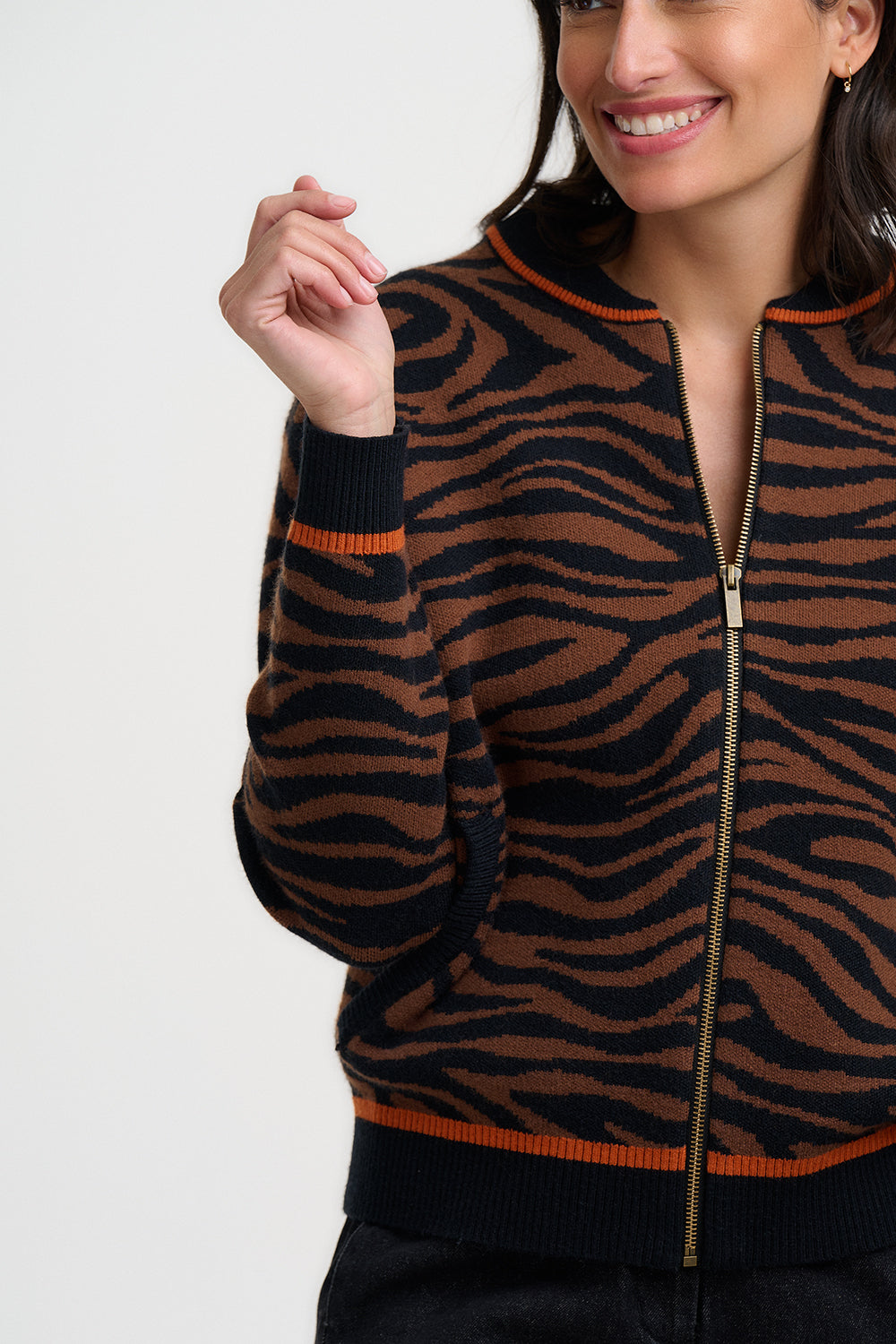 Woman wearing the brown and black tiger pattern Solana knitted bomber jacket from Sugarhill Brighton with orange accents on a white background