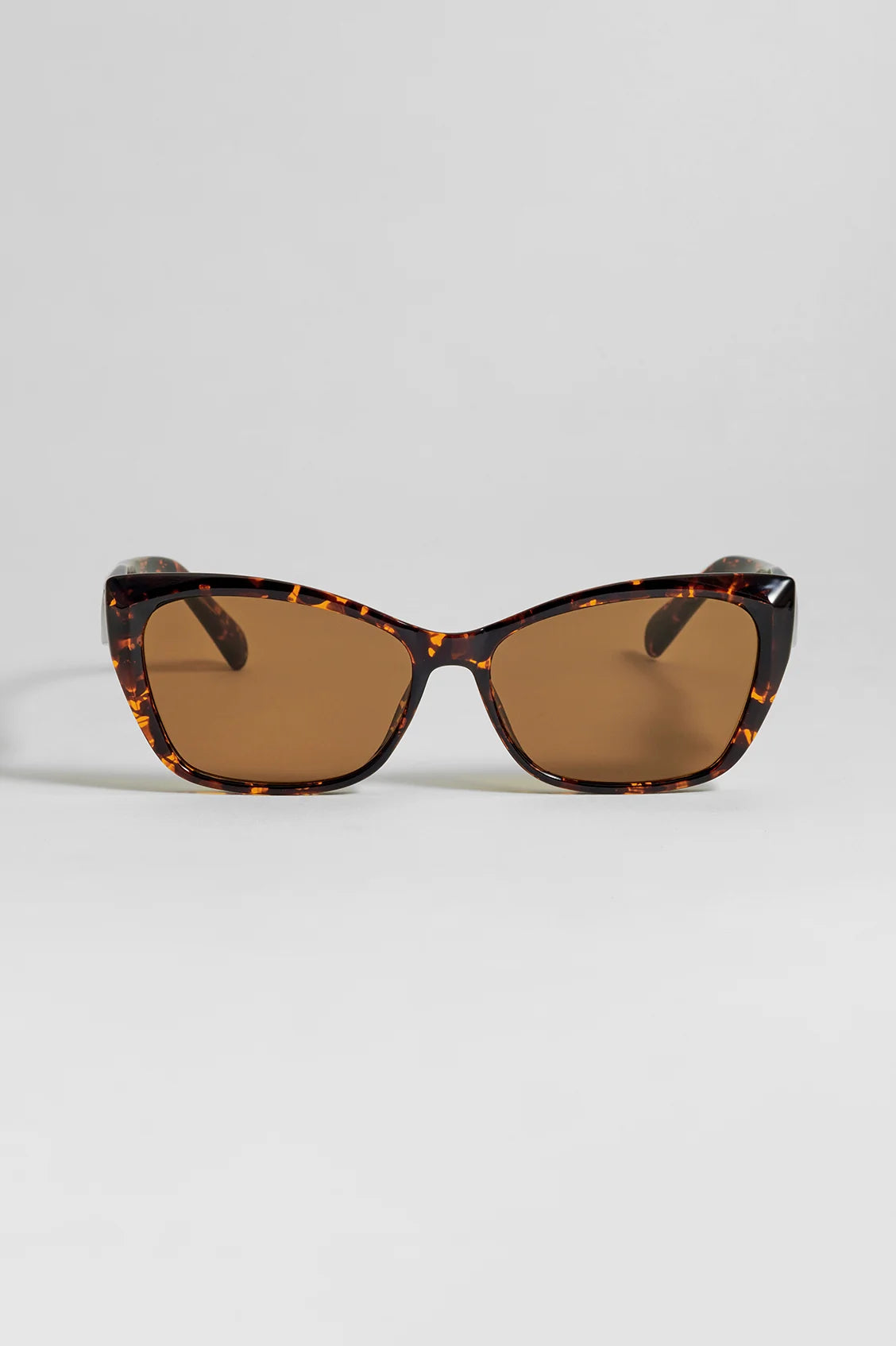 Cat-eye sunglasses from Estella Bartlett with tortoiseshell frame and brown lenses on a light gray background