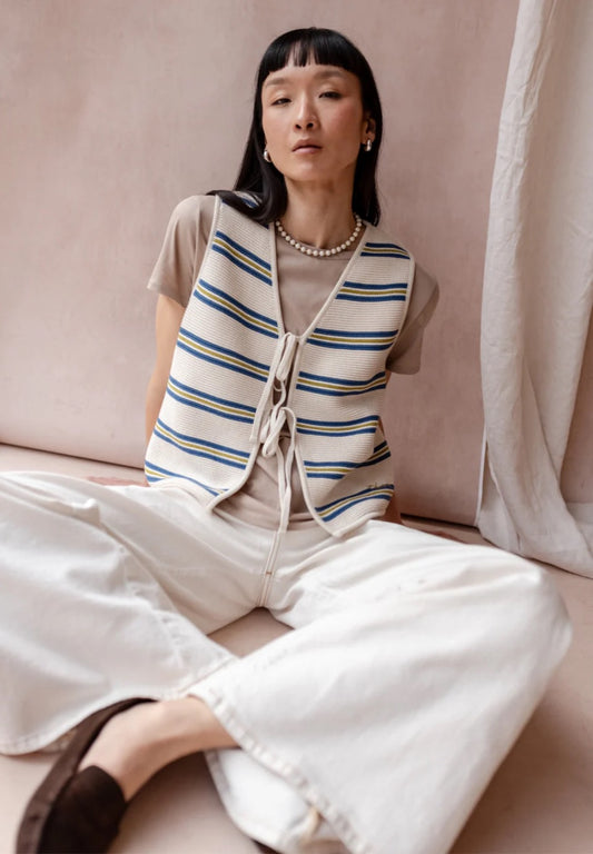 Knitted sleeveless vest from TBCo in cream, with fine horizontal stripes in dark blue and pistachio green. Made from 100% high-quality cotton. With two front ties for adjustable styling.