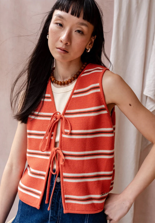 Knitted sleeveless vest from TBCo in a bold orange, with fine horizontal stripes in cream and dark brown. Made from 100% high-quality cotton. With two front ties for adjustable styling.