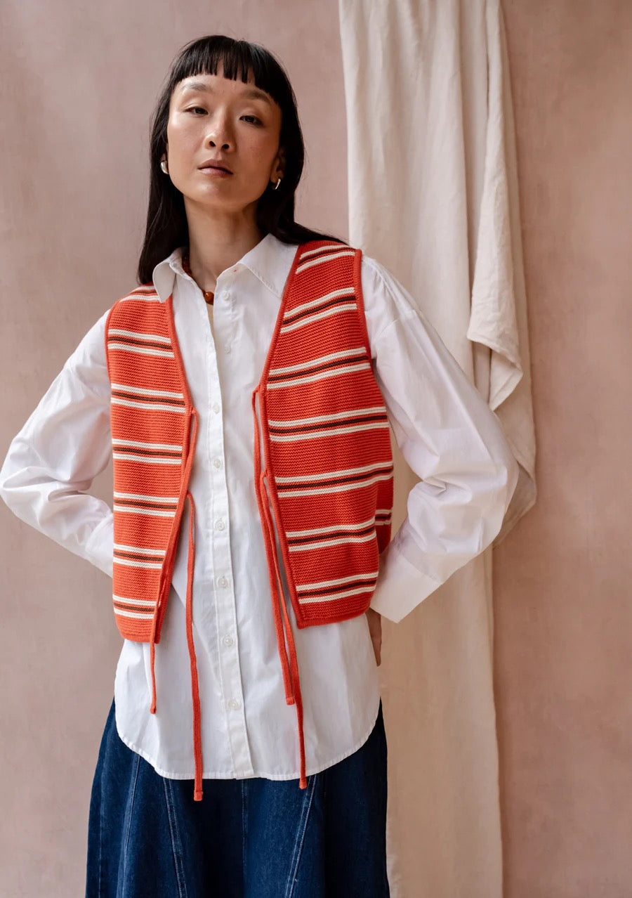 Knitted sleeveless vest from TBCo in a bold orange, with fine horizontal stripes in cream and dark brown. Made from 100% high-quality cotton. With two front ties for adjustable styling.