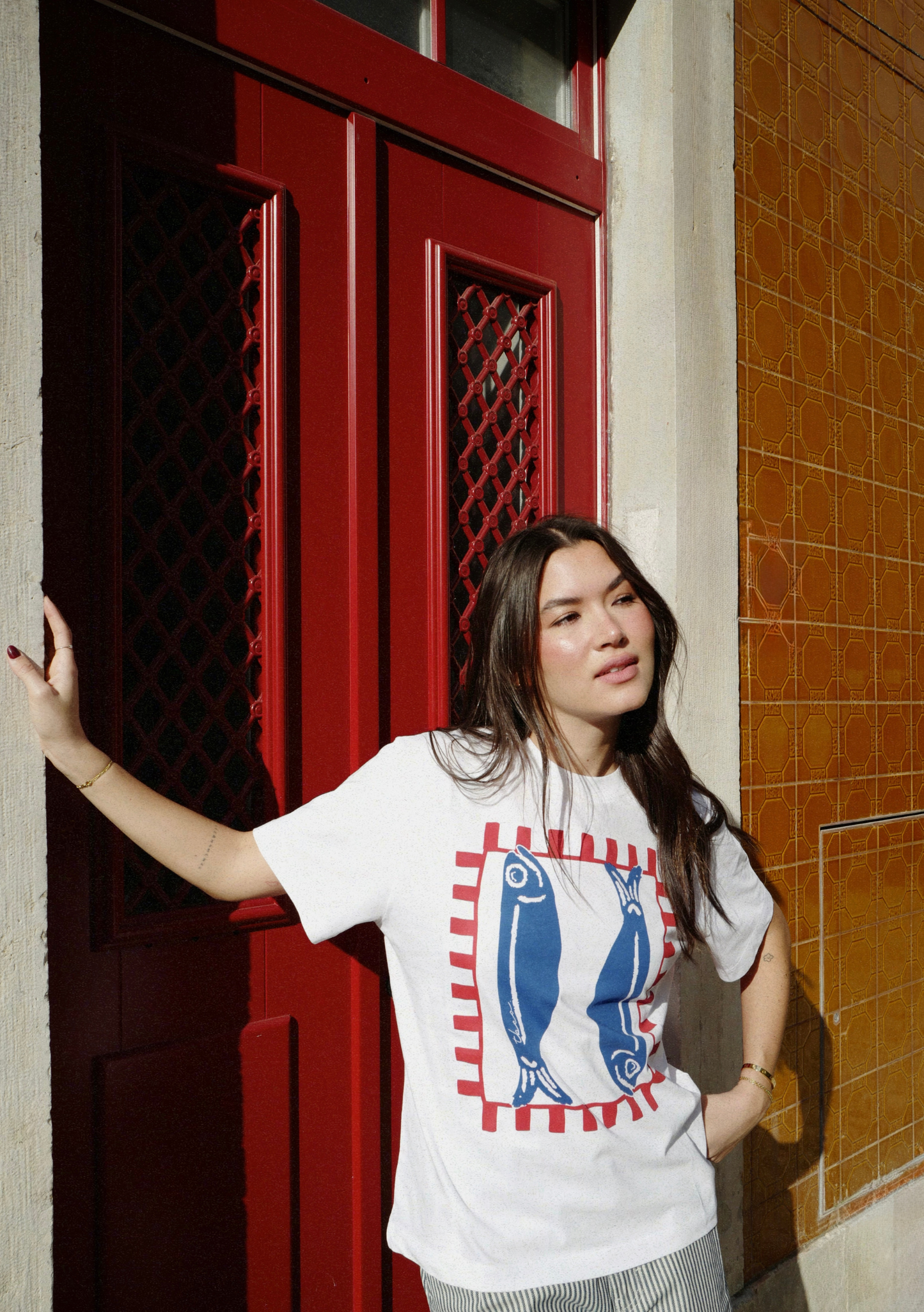 Woman wearing a white t-shirt with a graphic fish motif, standing in front of a red door.