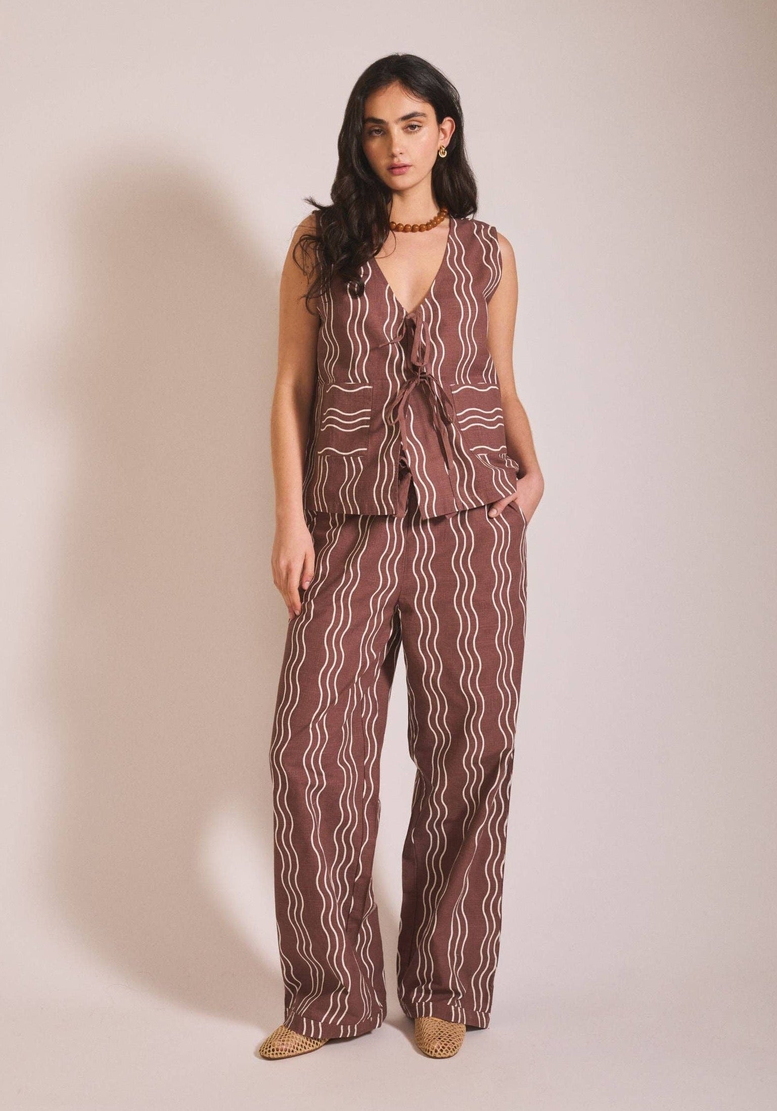 Woman wearing a patterned sleeveless top and pants on a beige background
