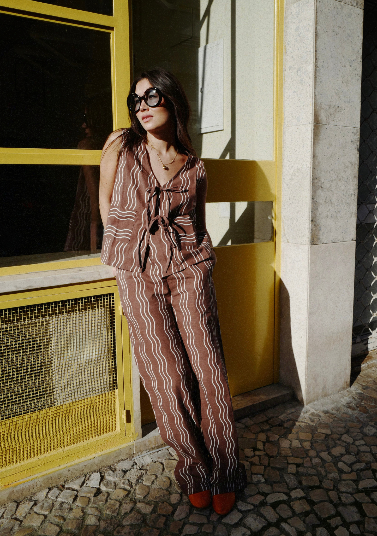 Woman in a patterned outfit standing in front of a yellow wall.